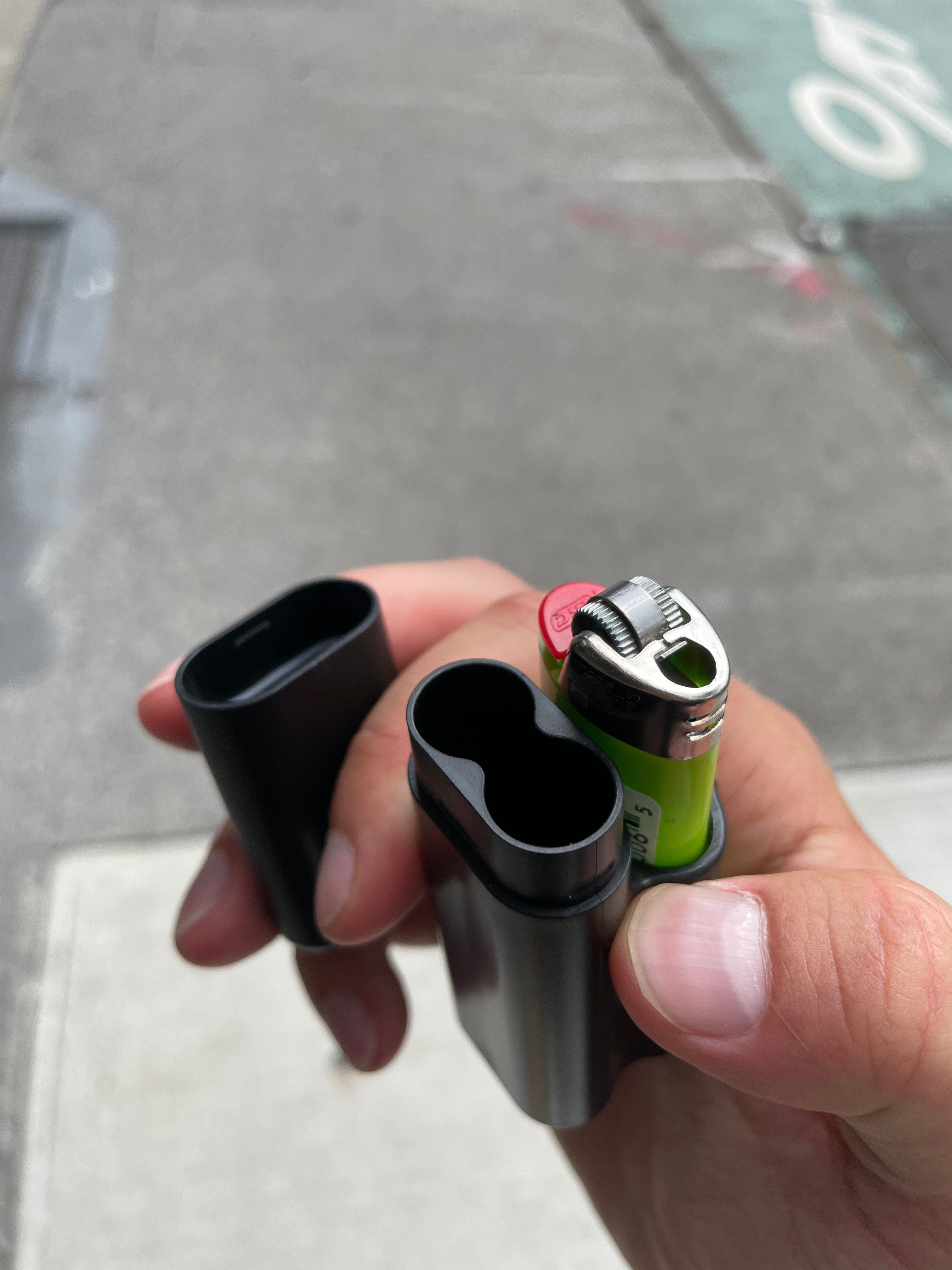 A hand holds The Clinger Stage 2 Dual Joint Holder, showcasing its sleek, black design against a blurred backdrop.