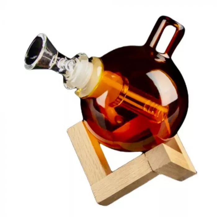 Angled view of the teal Art of Smoke Orb Bubbler resting in a wooden stand, showing its round amber glass body, mouthpiece and bowl.