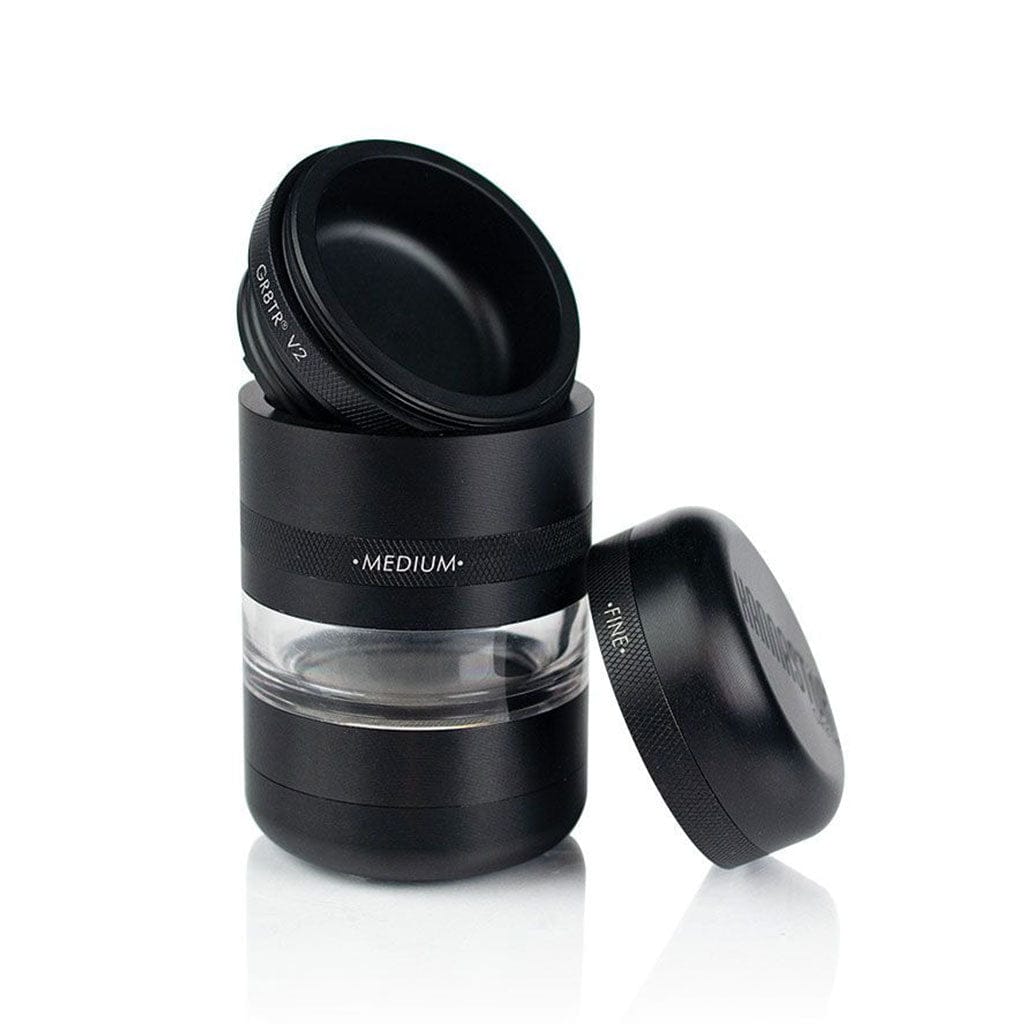 Three-quarter view of the black Ryot Gr8Tr Jar Body Grinder with its lid tilted atop the unit and a second cap leaning beside it on a white background