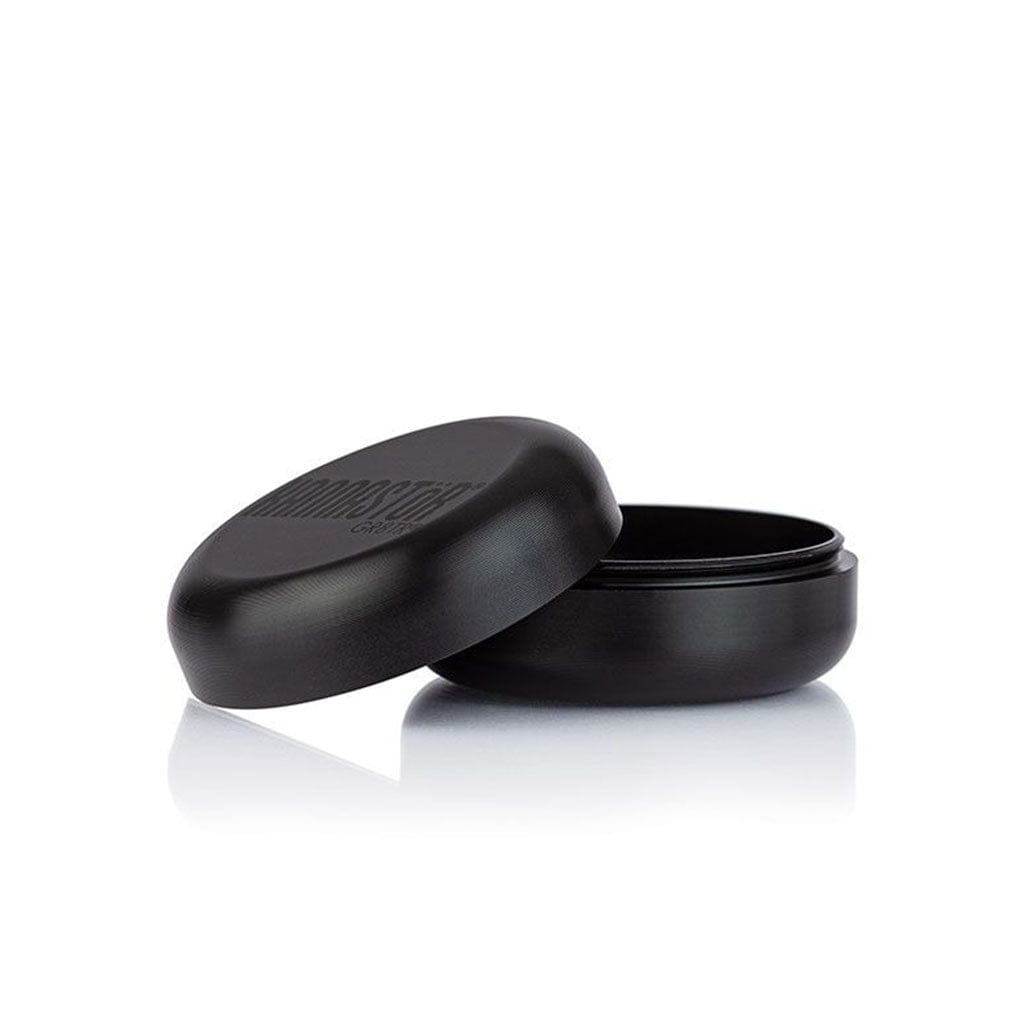 Low-angle three-quarter view of the black Ryot Gr8Tr Jar Body Grinder with its lid slightly ajar on a reflective white surface