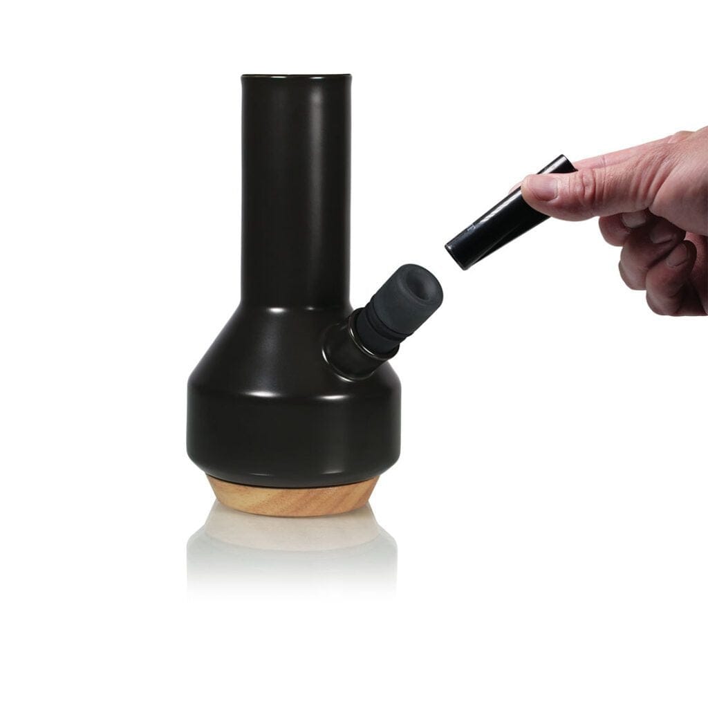 Angled studio shot of the black Ryot Ceramic Maple Traveller Pipe with its maple wood base and a hand holding the removable mouthpiece.