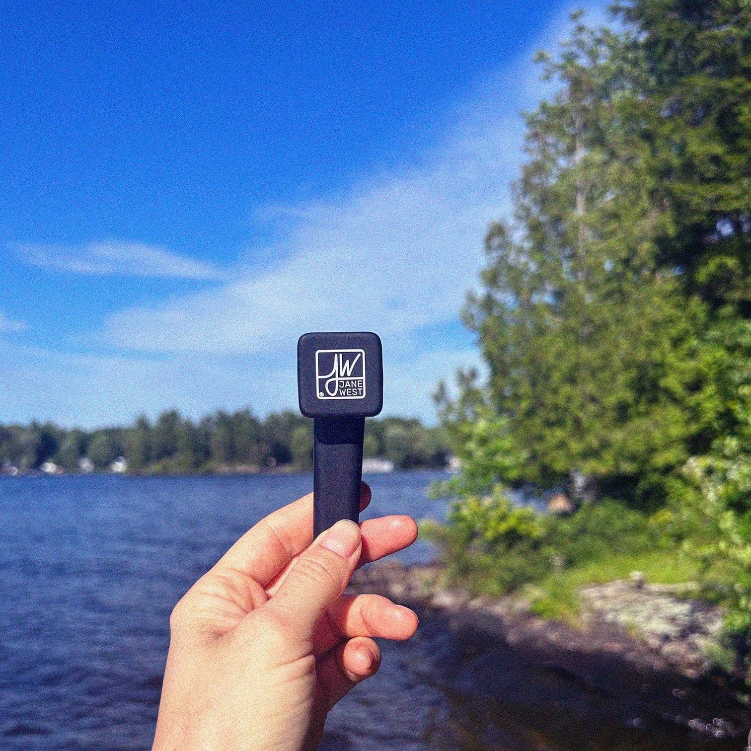 A hand holds The Outdoor Silicone Pipe against a blurred background of trees and water.