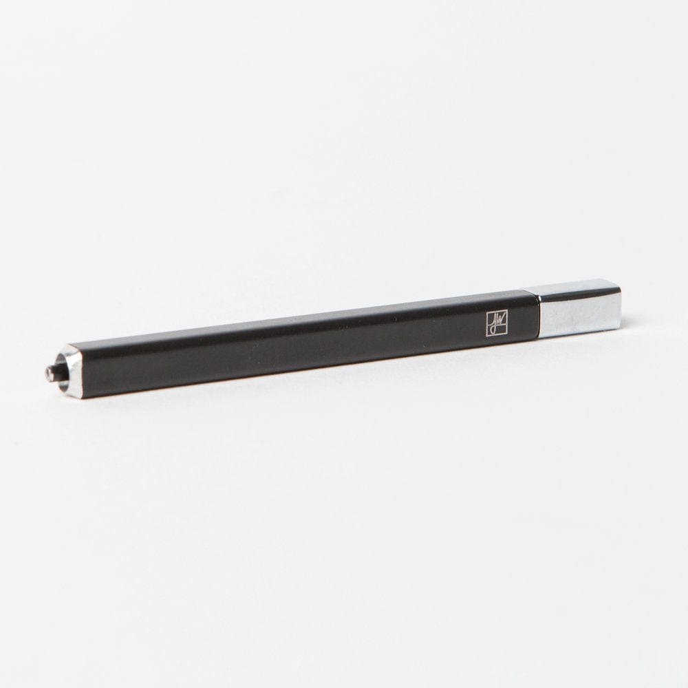 Angled close-up of The Solo, a slim black hexagonal pen with chrome ends resting on a white surface.
