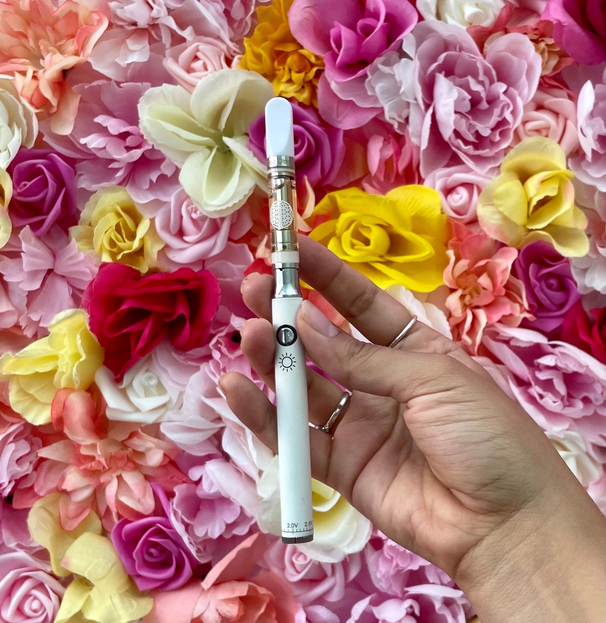 A close-up, angled view of the Day 510 Vape Battery against a vibrant pink floral background, highlighting its sleek, cylindrical shape.