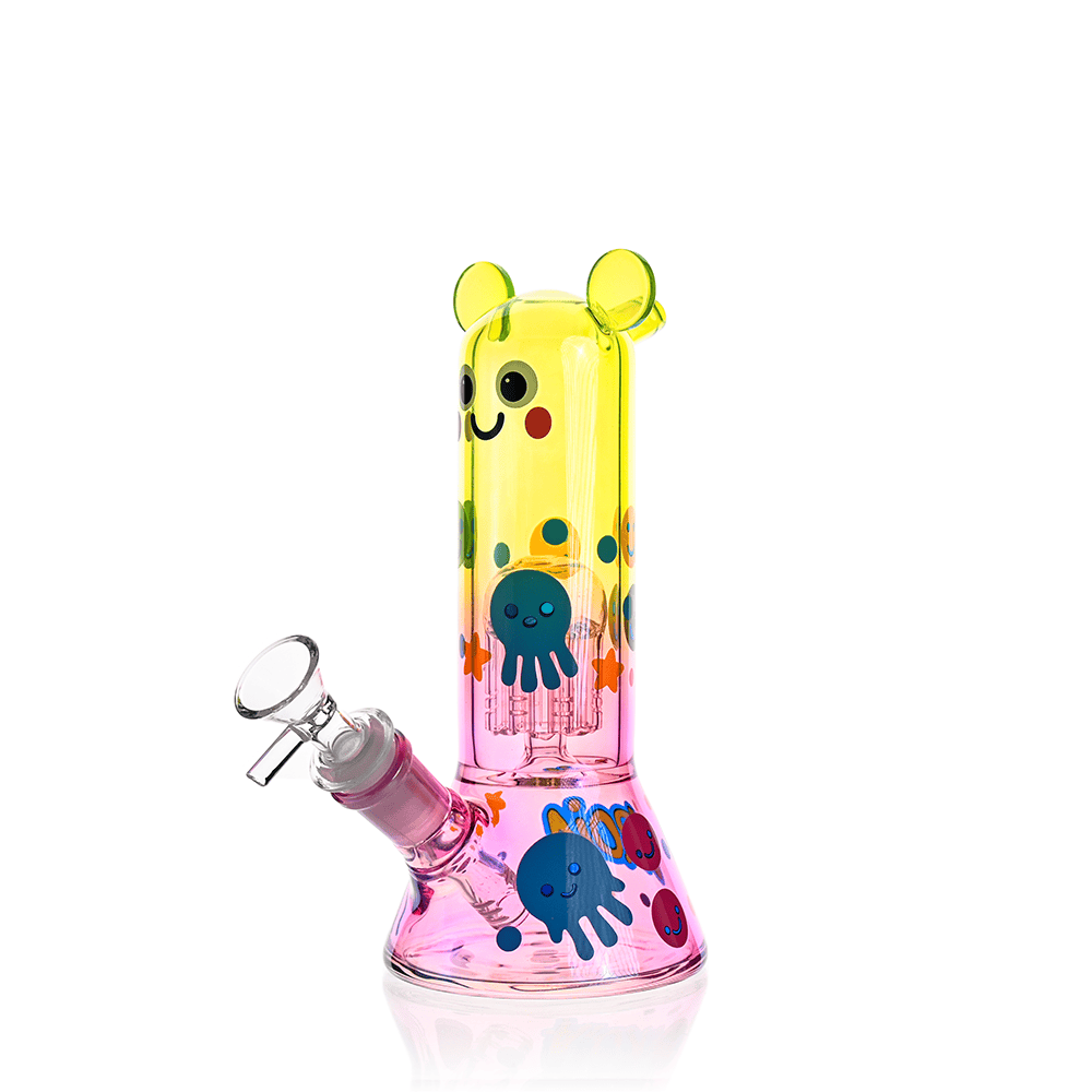 Front three-quarter view of the Croia Glass Cute Character Beaker Bong with Jellyfish Design | Croia Glass showing its yellow-to-pink gradient, smiling face and blue jellyfish decals.