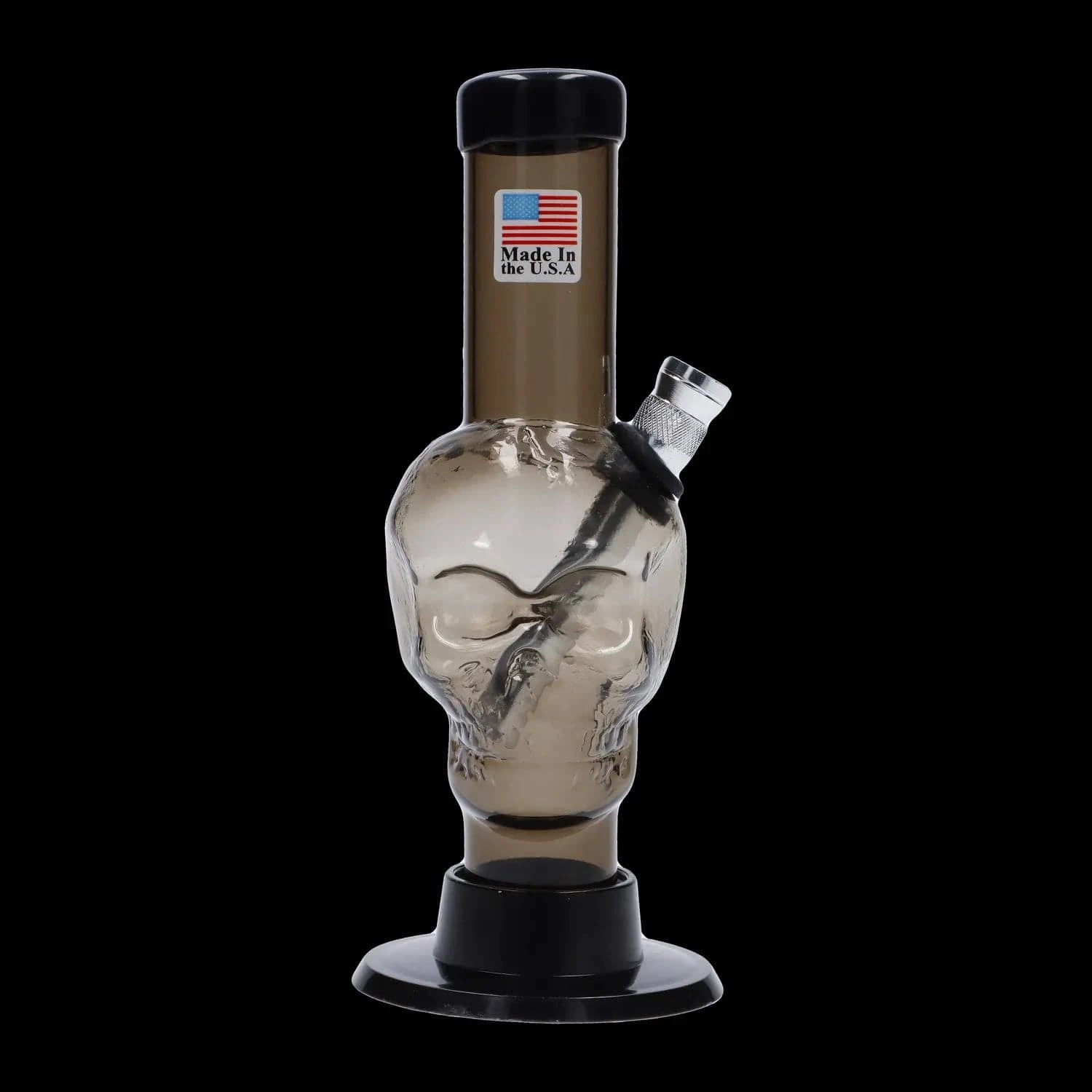 Front-facing close-up of the JM Plastics Mini Skull Base Acrylic Bong - 6 in. showing its clear smoke-tinted skull chamber, angled metal downstem, and black mouthpiece against a black background