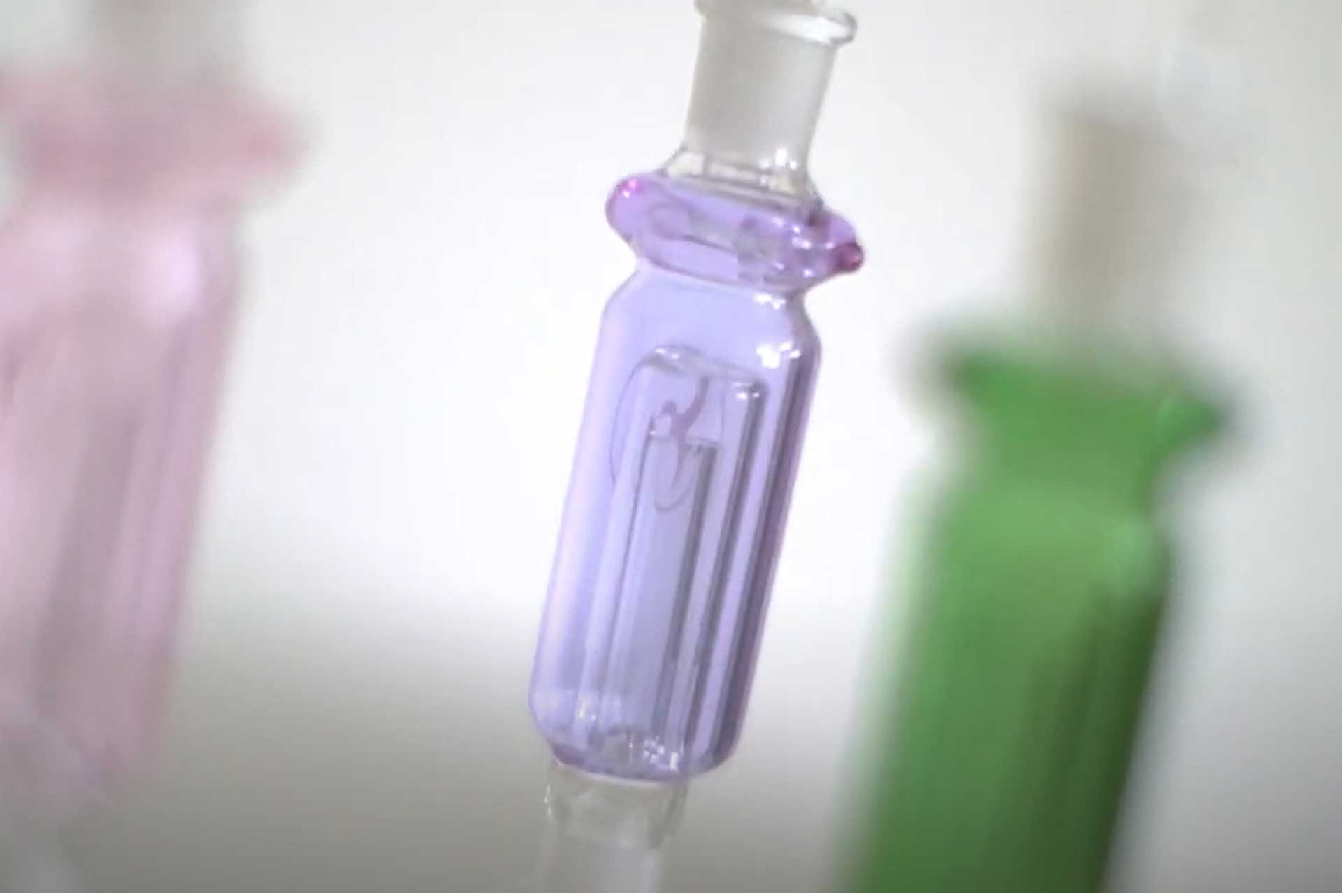Close-up of a purple-tinted glass tip on the Nectar Collector Wildbird Kit, shot at an angled close range with soft out-of-focus green and pink shapes in the background