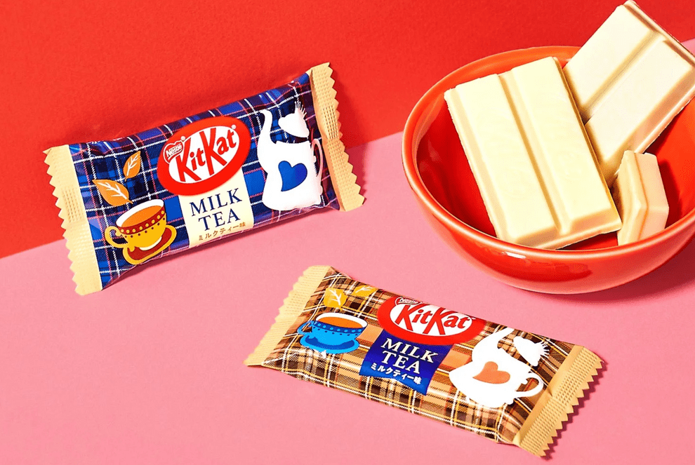 Close-up of a Japanese KitKat - Milk Tea bar with a patterned wrapper, positioned against a light-colored surface.