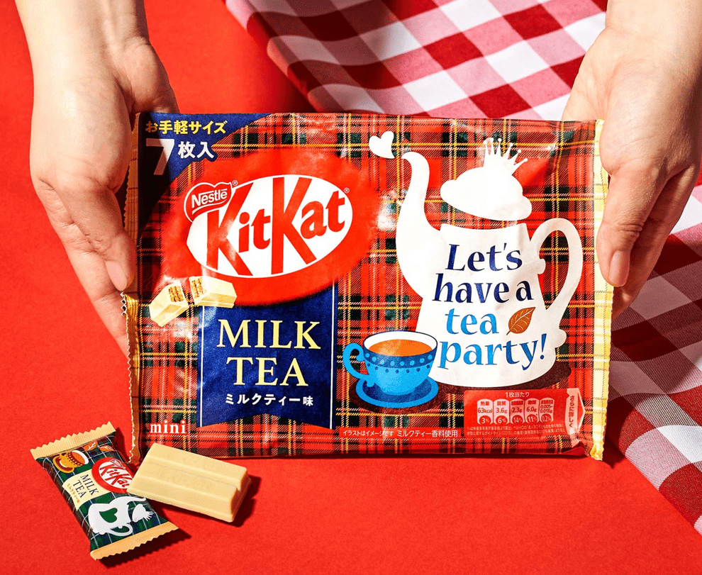 A close-up, angled view of a Japanese KitKat - Milk Tea wrapper with Japanese text alongside a steaming teacup.