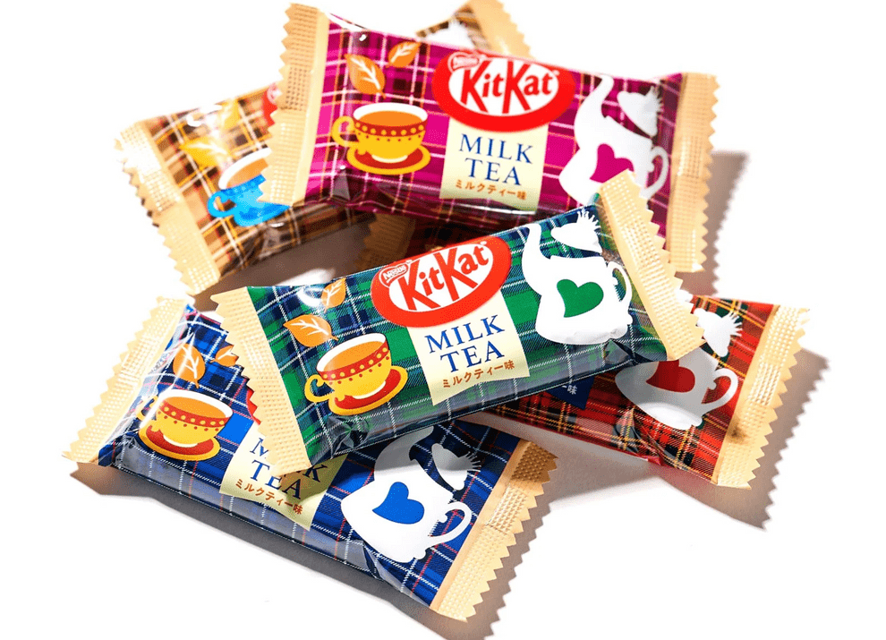 A close-up, angled view of a Japanese KitKat - Milk Tea bar with patterned packaging against a white background.