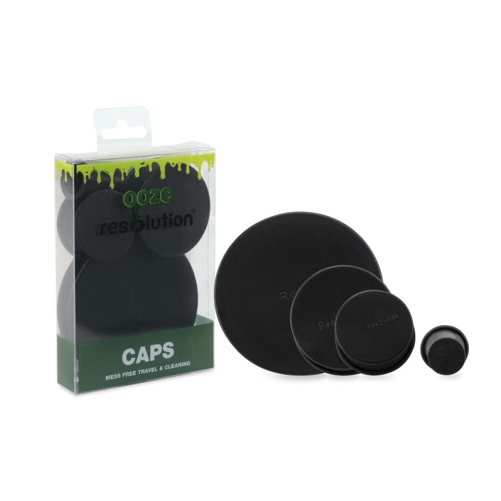 Packshot showing four black Ooze Resolution Caps of graduated sizes arranged front-right of their clear retail packaging on a white background.