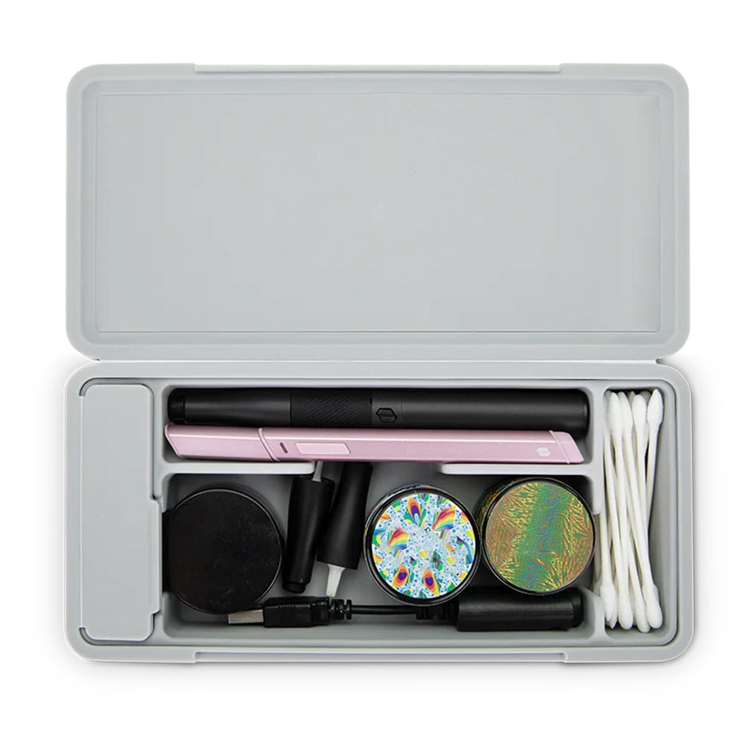 Top-down view of a gray travel case open to reveal a pink and black Puffco Pivot Travel Case with accessories neatly arranged, including cotton swabs, two colorful round containers, chargers, and small black components.