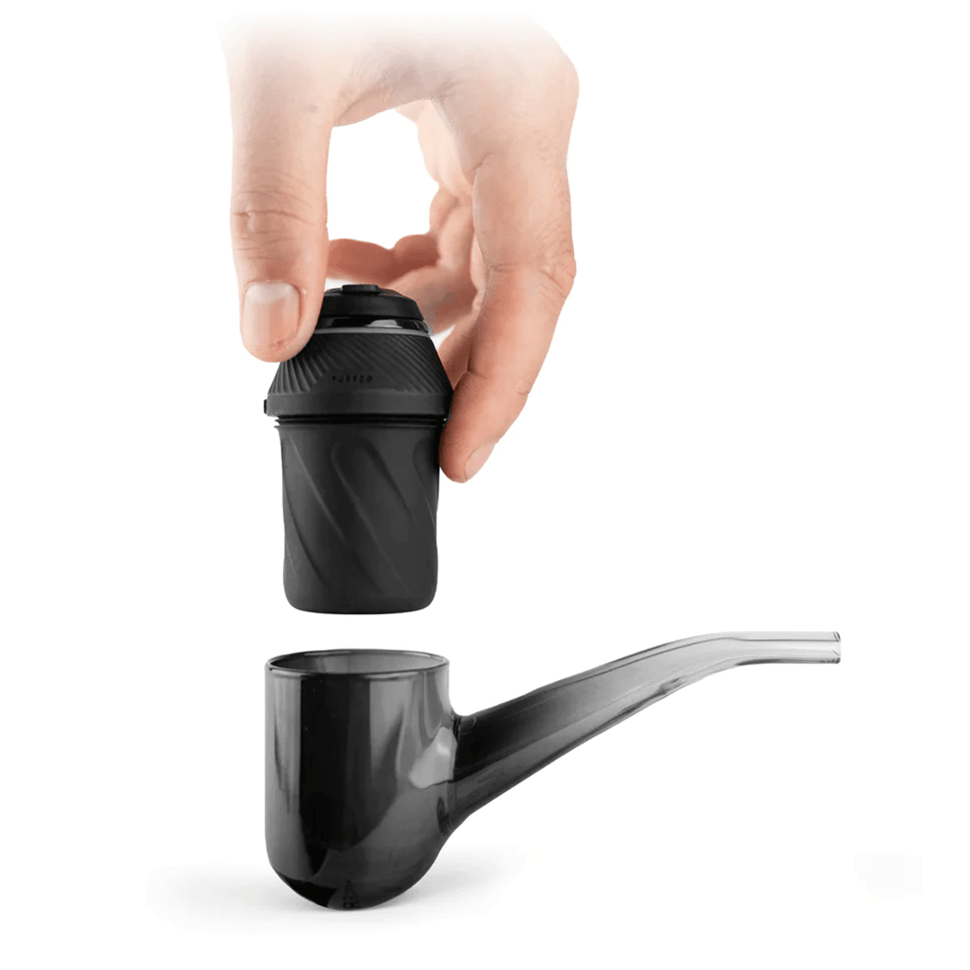 Top-down view of a hand lowering the black Puffco Proxy chamber into a glossy black pipe bowl against a white background