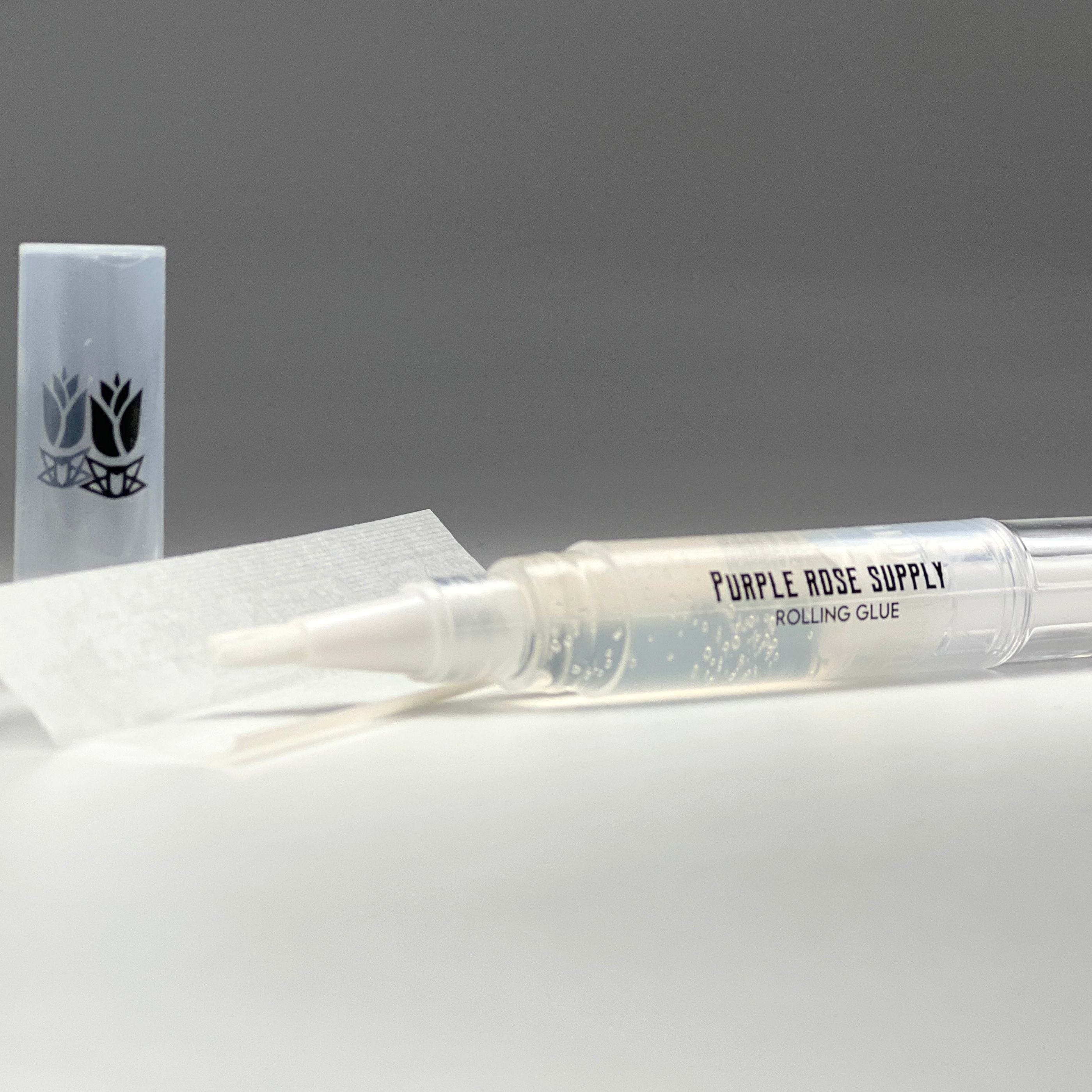 Close-up, angled view of the Cannagar & Blunt Rolling Glue - 4ml pen lying on white paper with a gray backdrop.