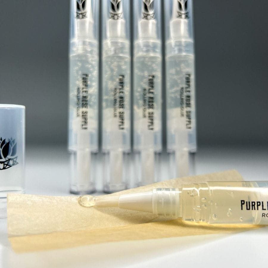 Close-up of a Cannagar & Blunt Rolling Glue - 4ml pen tip dispensing a clear droplet onto rolling paper with four filled pens blurred upright in the background