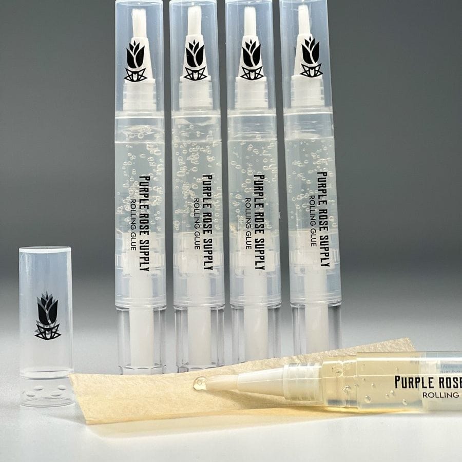 Close-up of five upright Cannagar & Blunt Rolling Glue - 4ml pens with clear gel and one pen tipped onto a paper strip on a gray background.