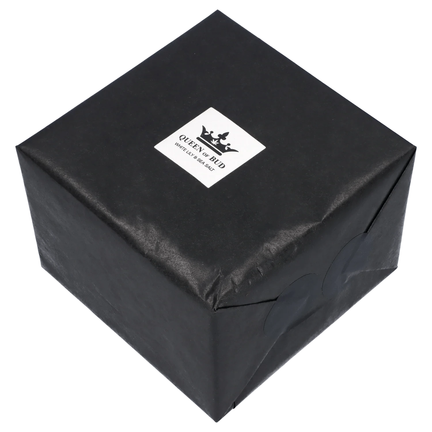 Angled top-down view of a black wrapped gift box with a white square label reading "Queen of Bud Candle."