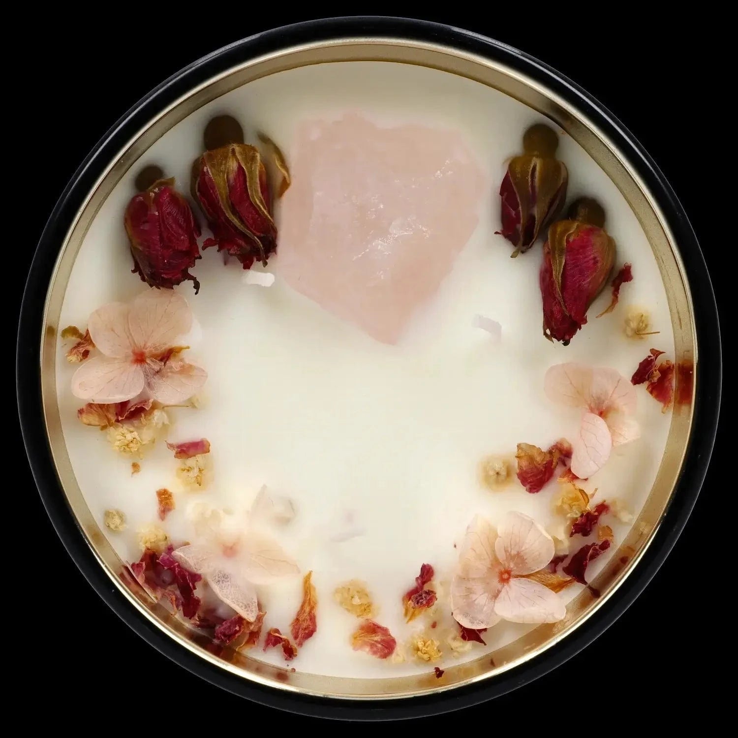Top-down view of the Queen of Bud Candle showing white wax topped with a central pale pink crystal and scattered dried pink and red flower petals.