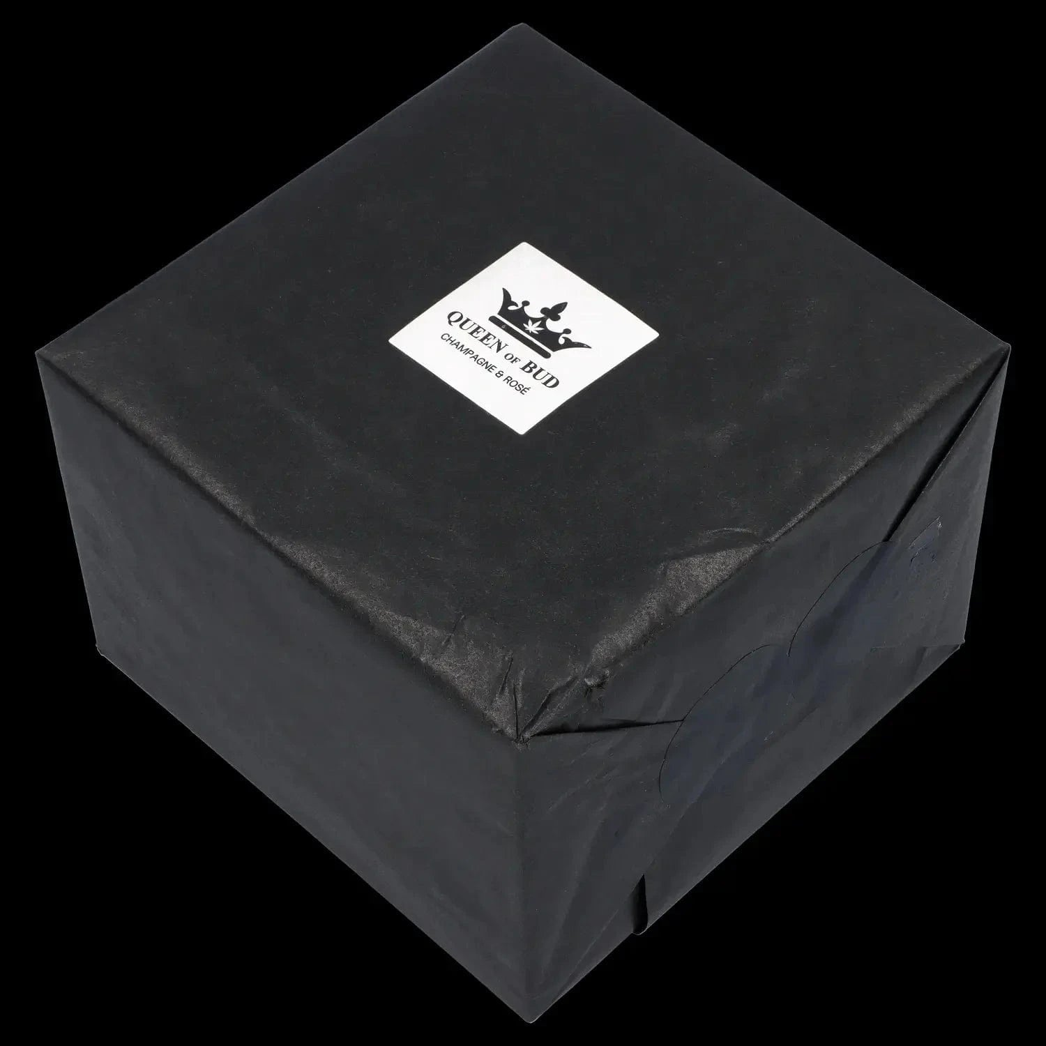 Angled top-down view of a black gift-wrapped box featuring a centered white label reading Queen of Bud Candle.