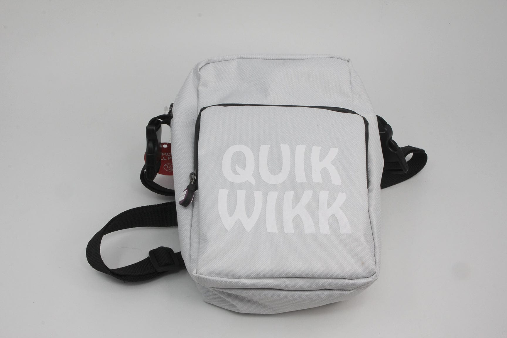 Front-facing shot of a white Quik Wikk Shoulder Cross Body Bag with front zip pocket and black strap laid flat on a light gray background