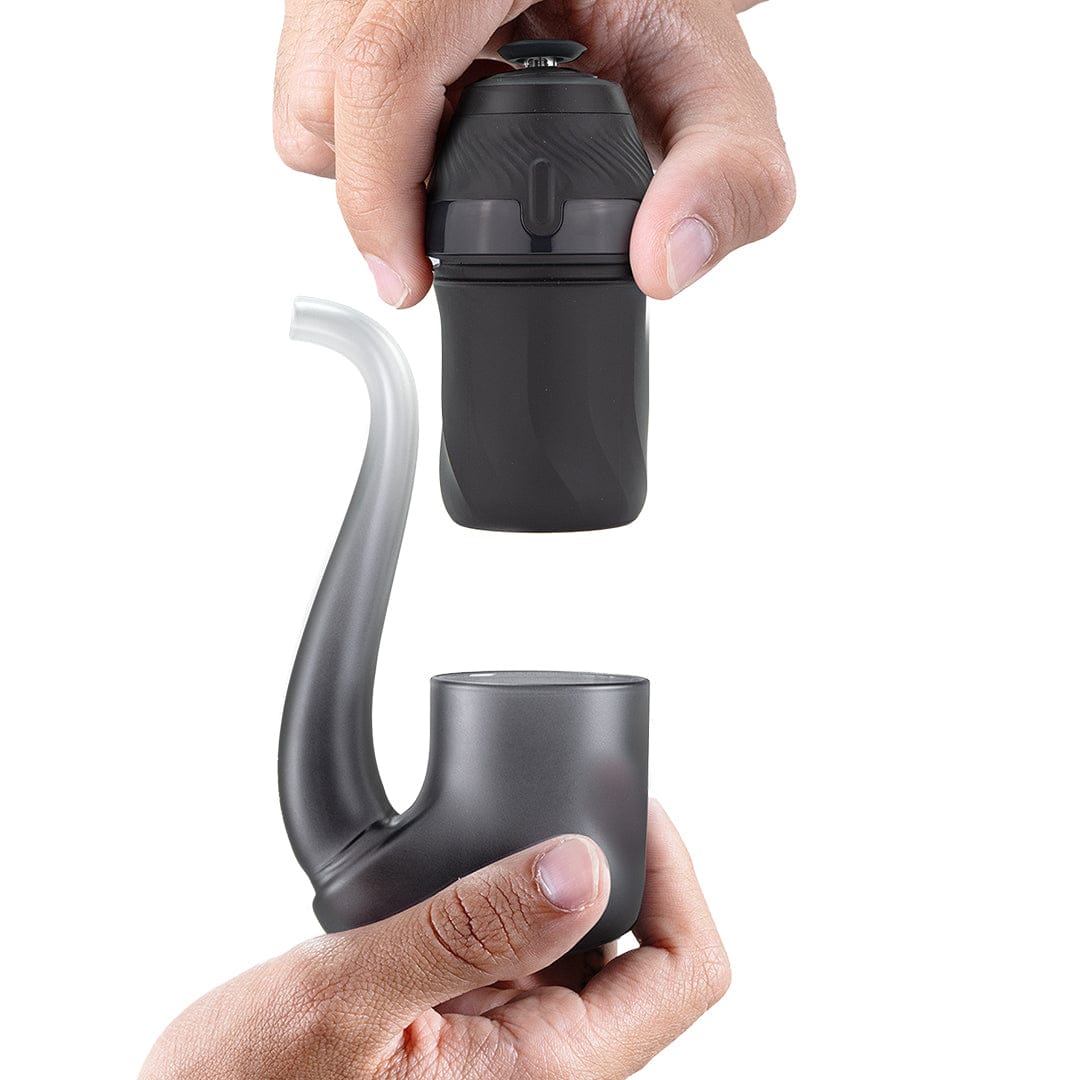 Hands assembling a matte black Puffco New Proxy Vaporizer, top piece held above the curved pipe-shaped base on a white background