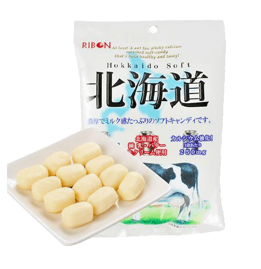 A close-up, slightly angled view of several individually wrapped pieces of Real Hokkaido Milk and Cream Calcium Enriched Soft Candy on a clear plastic background.