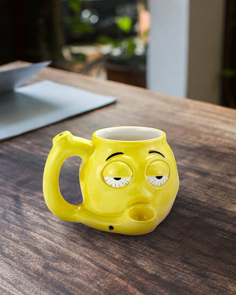 A close-up, angled view of the Stoned Emoji Pipe Mug & Stash Jar Bundle, featuring a yellow, smiling ceramic mug with a pipe-like form.