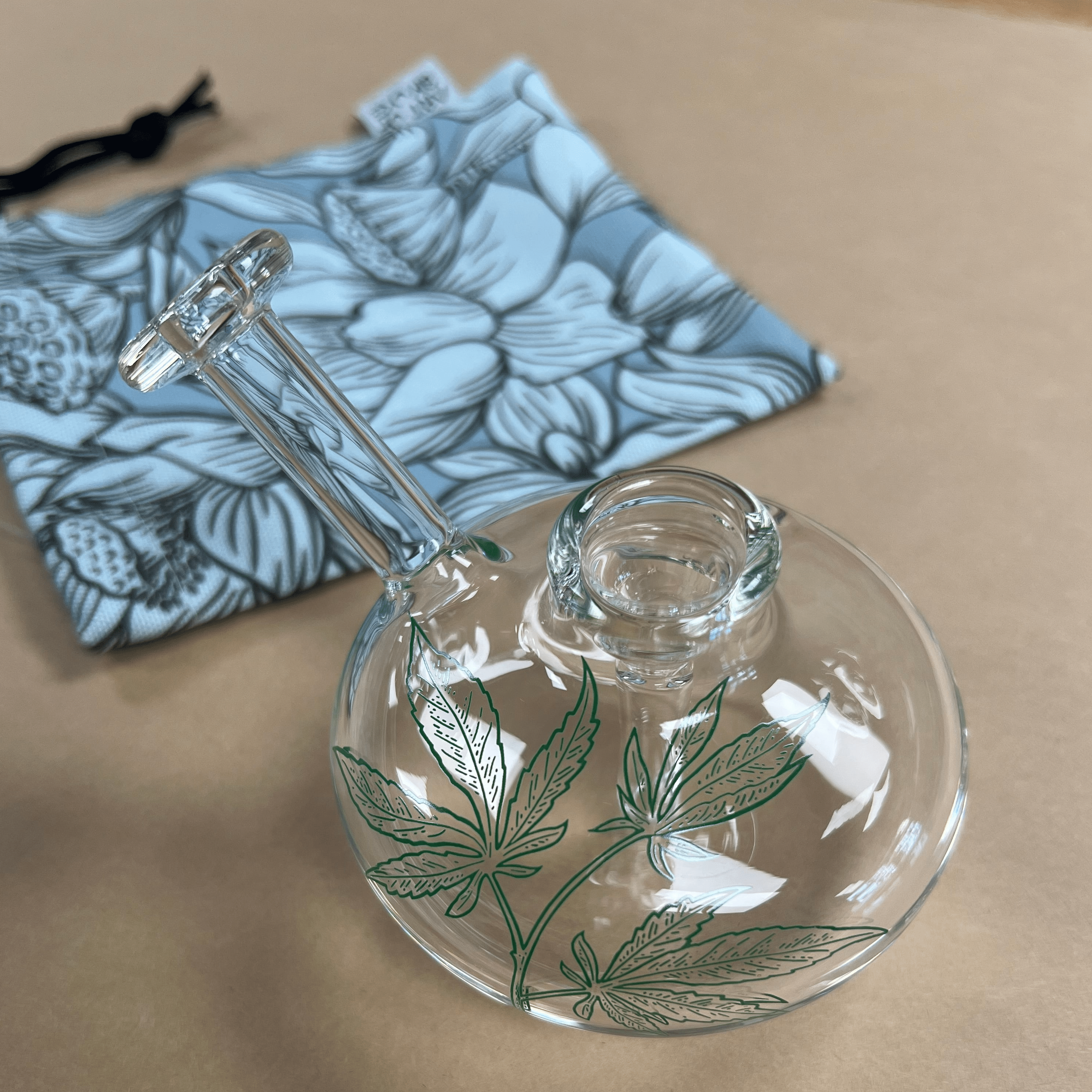 A close-up shot of the Lil Sprout Bubbler, showcasing its clear glass construction against a patterned blue pouch.