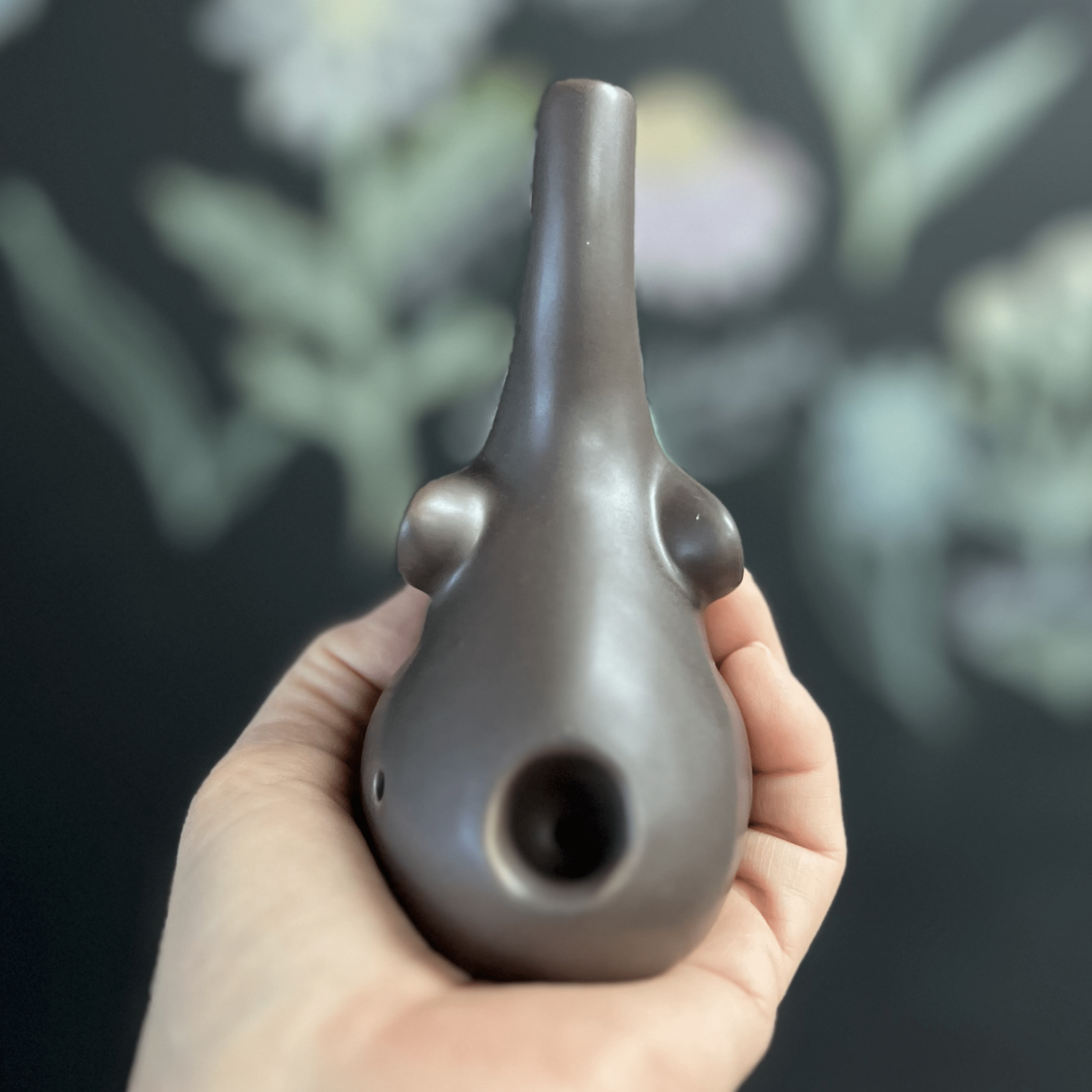 A hand holds the dark-colored Baby Elephant Sherlock Pipe, showcasing its sculpted form against a blurred green background.