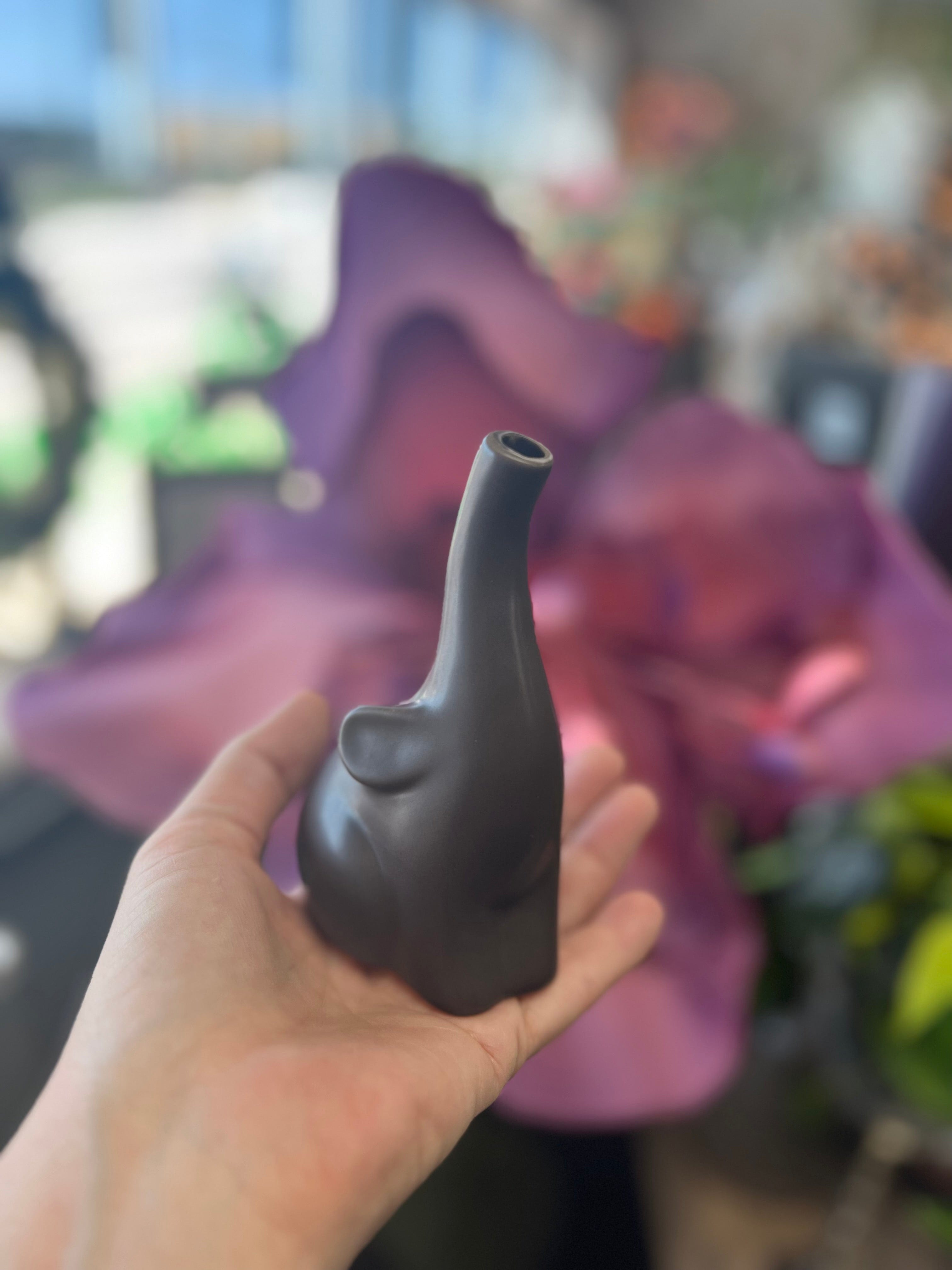 A hand holds the miniature Baby Elephant Sherlock Pipe, its detailed design highlighted against a blurred purple background.