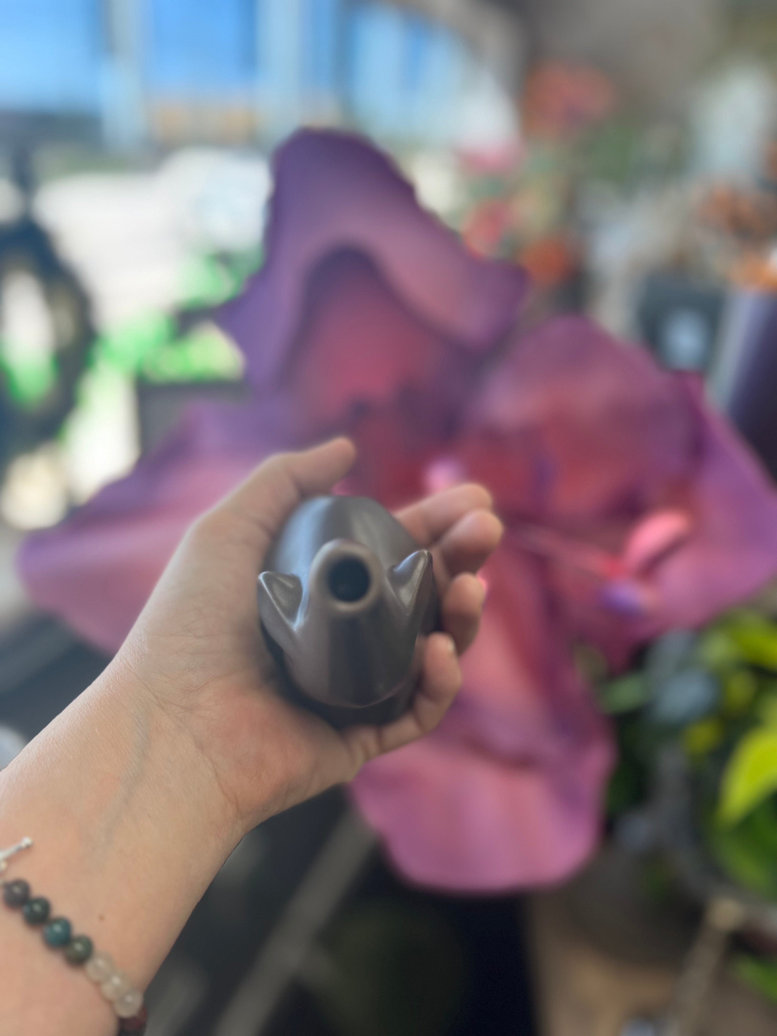 A hand holds the small, dark-colored Baby Elephant Sherlock Pipe against a blurred, vibrant purple background.