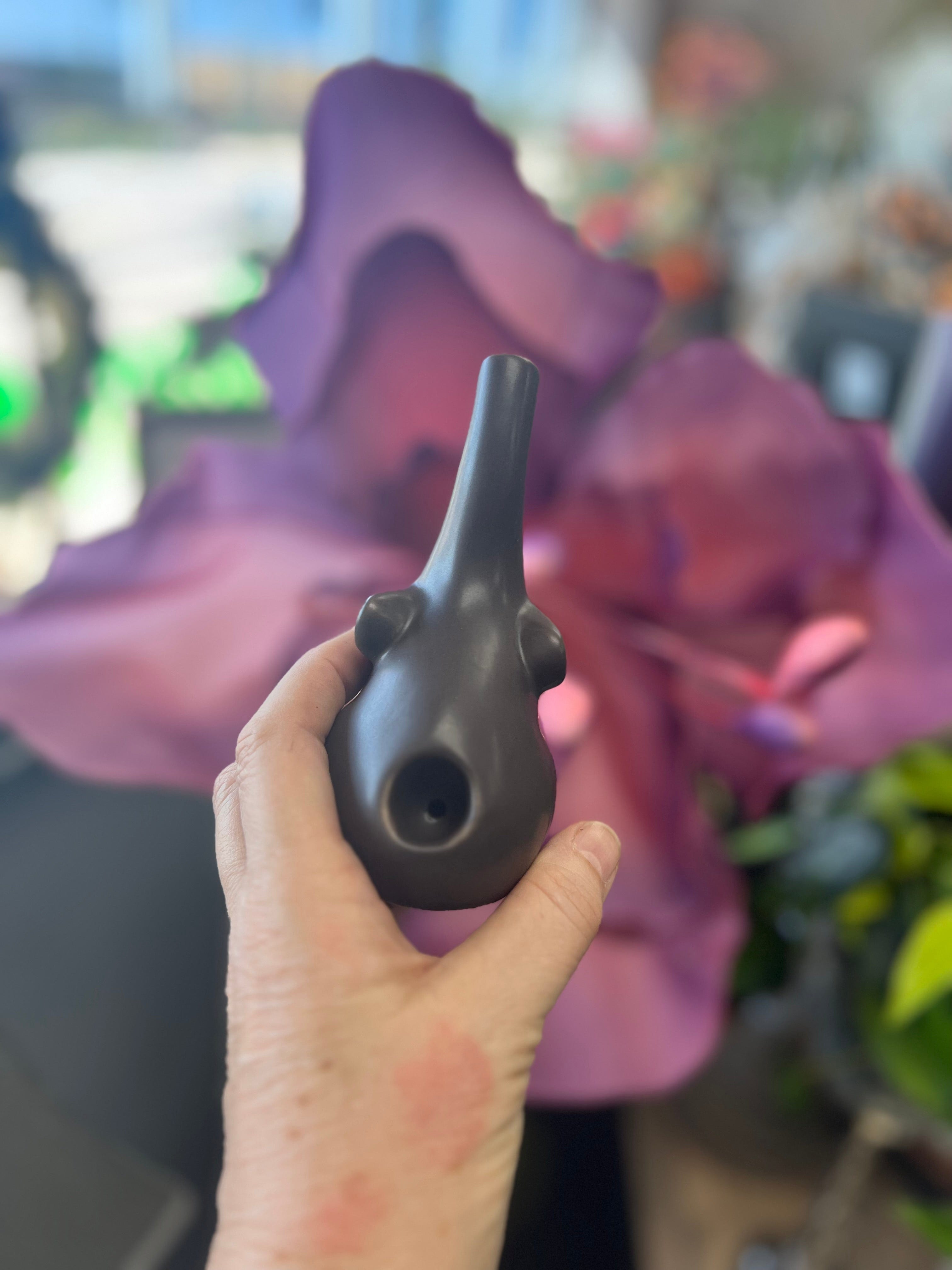 A hand holds the dark-colored Baby Elephant Sherlock Pipe, with a purple backdrop softly blurred behind it.