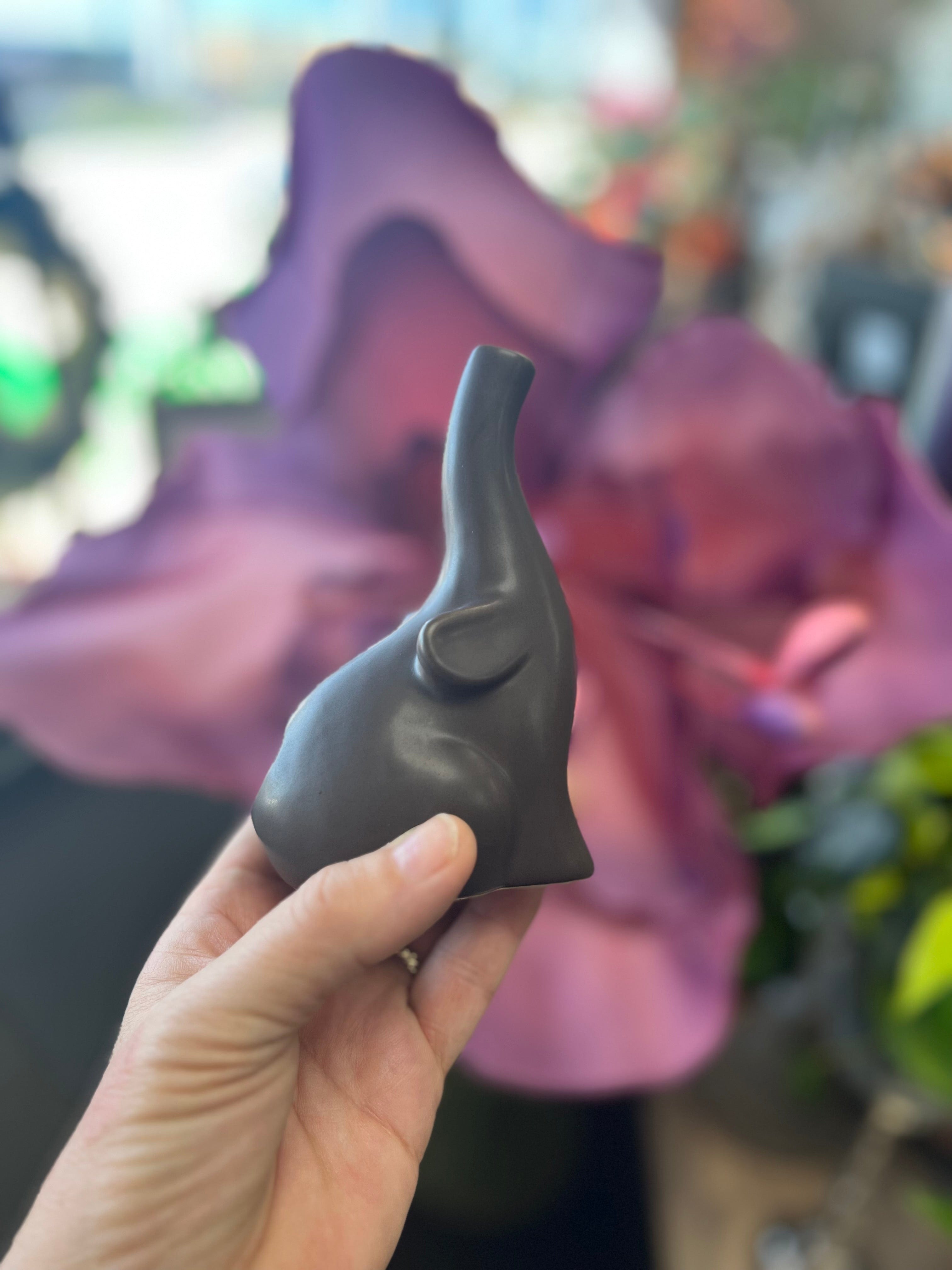 A hand holds the small Baby Elephant Sherlock Pipe against a blurred purple background, showcasing its unique sculpted design.
