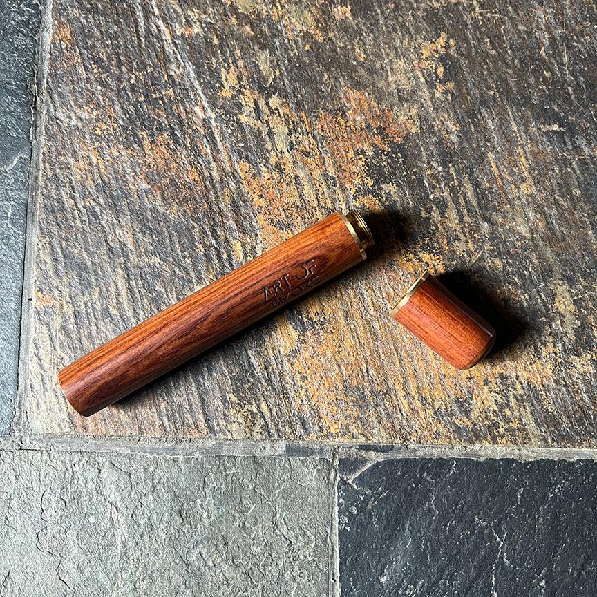 A close-up shot of the Rosewood Doob Tube lying on a textured gray surface, displaying its warm wood grain.