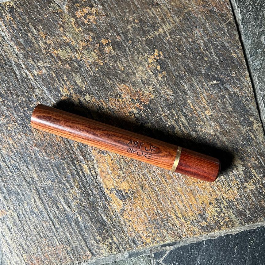 Close-up of the Rosewood Doob Tube, a dark wood case with a smooth, cylindrical shape, resting against a textured gray background.