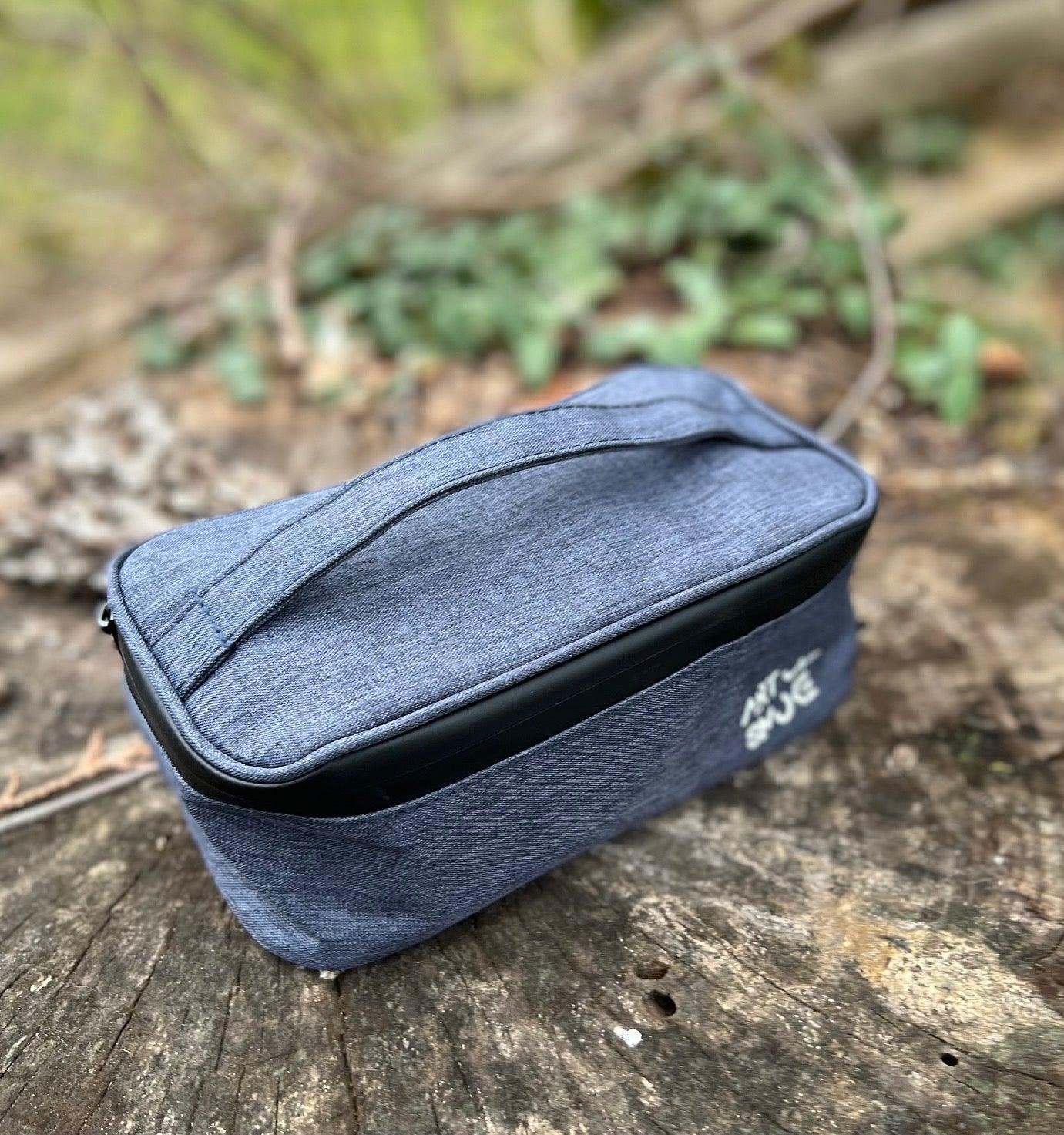 A slightly angled view of the Travel Odor Proof Case, a dark blue zippered bag resting on a bed of dry green plants.