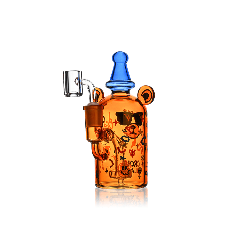 Front-lit studio shot of the Croia Glass Cool Teddy Bear Dab Rig with Showerhead Perc | Croia Glass, an orange glass teddy-shaped rig with blue top and black graphic sunglasses, shown upright on a white background