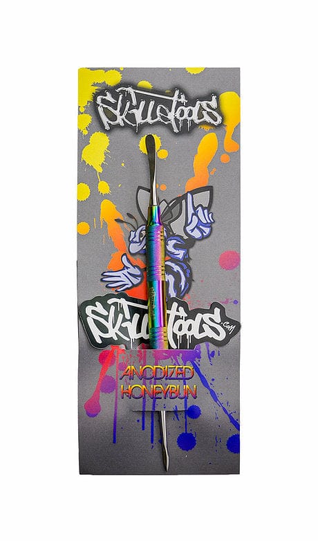 Front view of the Anodized Honeybun Dabber against a grey backdrop with bright yellow and blue paint splatters.