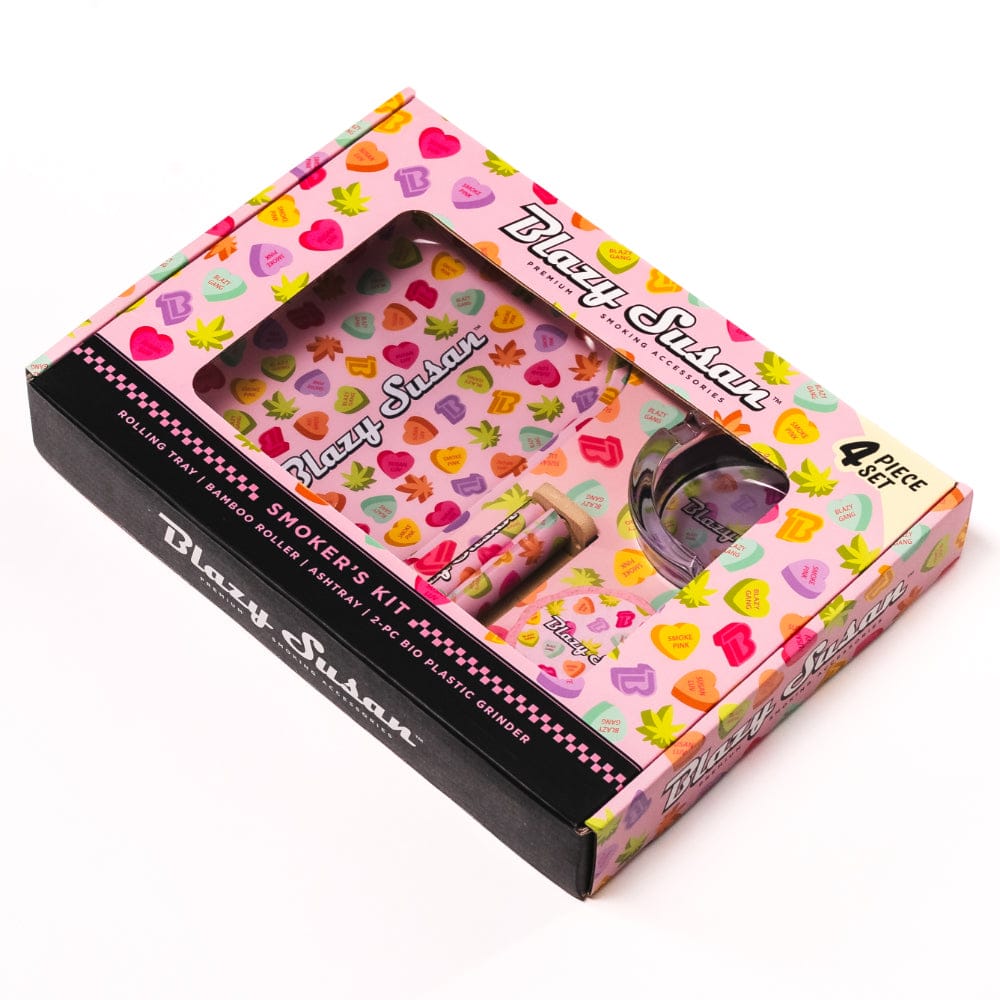 Angled top view of the pink, heart-and-leaf patterned Blazy Smoker's Kit in its windowed box showing the tray, roller and grinder.