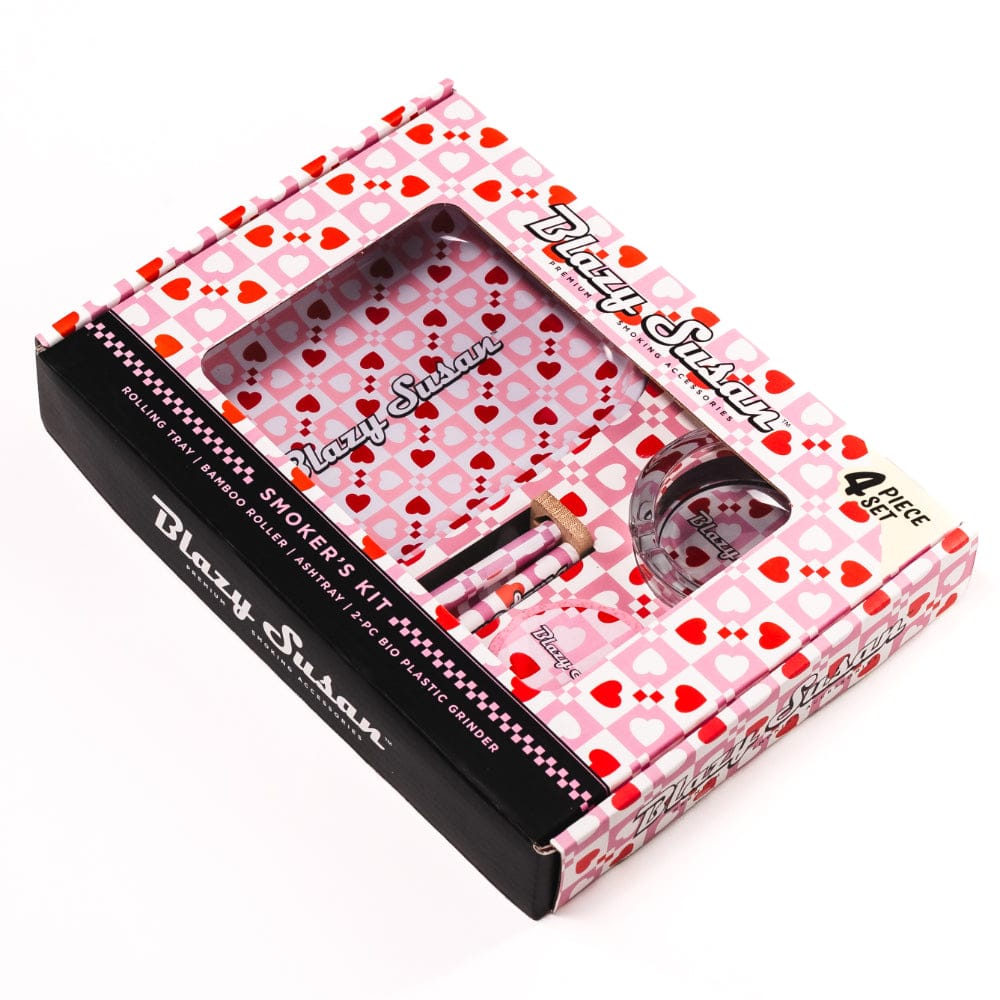 Angled top view of the pink heart-patterned Blazy Smoker's Kit box showing its windowed tray, roller, grinder and matching heart-print accessories.