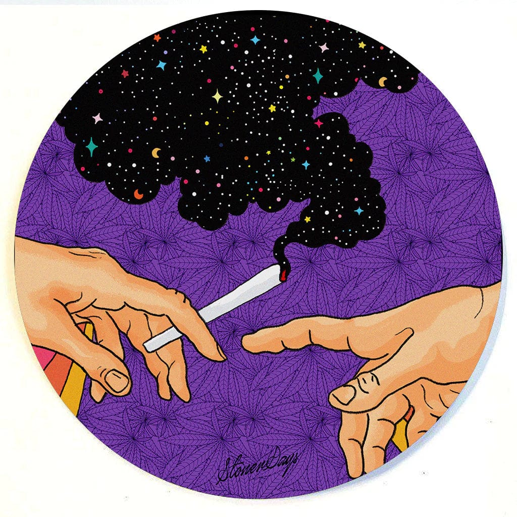 A close-up, overhead view of hands holding a lit joint above the patterned surface of the Stonerdays Round Dab Mats.