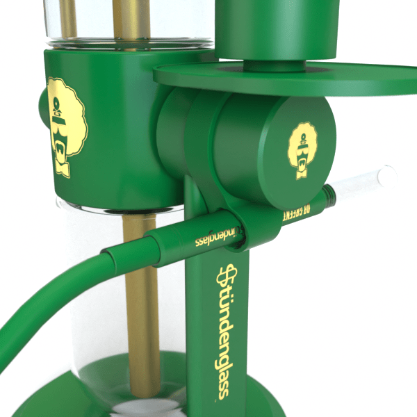 Close-up angled view of the green Hose Clip - Green attached to a Stündenglass rig, showing the round clamp, tubing, gold logo accents, and glass chamber.