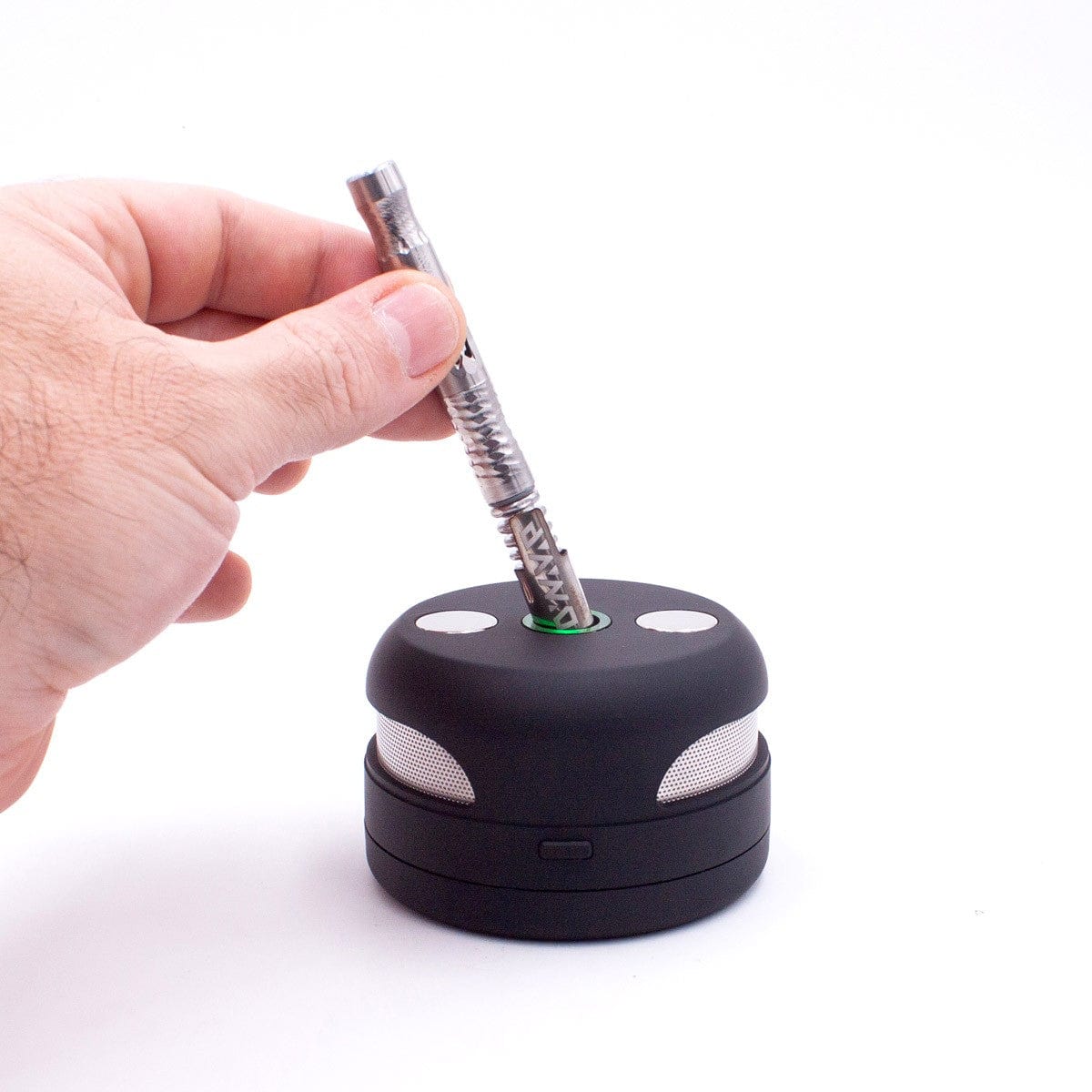 A hand holds a lit joint over the circular top of the UFO Induction Heater, resting on a white surface.
