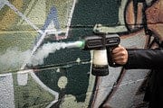 Side view of a person holding the black SeshGear Super Smoker Smoke Thrower Bong - 1500Mah / Black against a graffiti-covered wall.