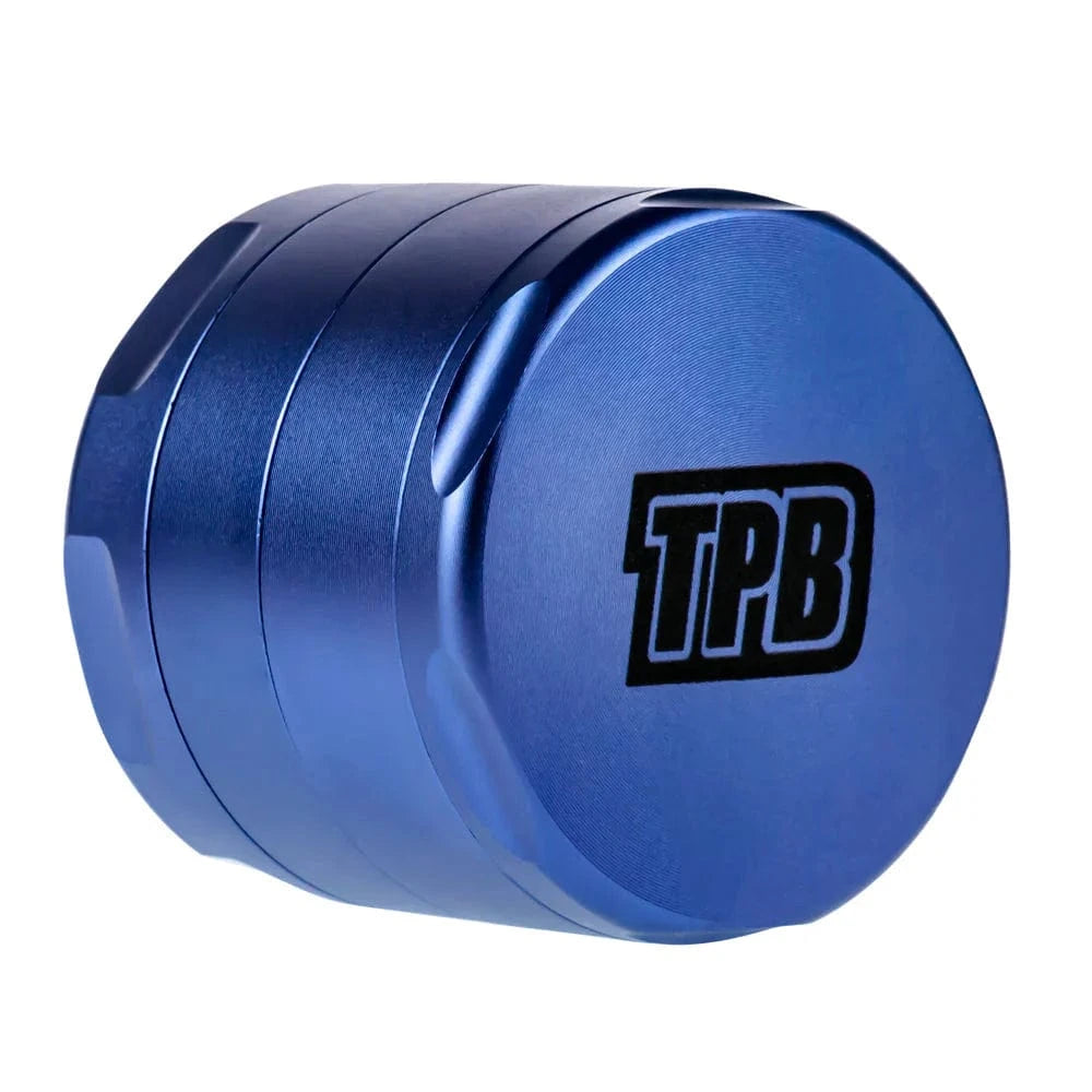 Angled close-up of a blue Famous X Trailer Park Boys Grinder - Assorted Colors showing its stacked metal chambers and black "TPB" logo.