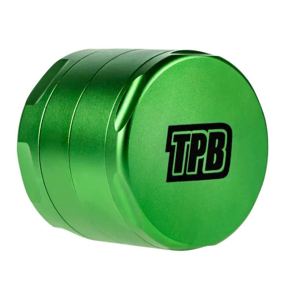 Angled close-up of a metallic green Famous X Trailer Park Boys Grinder - Assorted Colors showing its ridged stacked chambers and black "TPB" logo on the lid