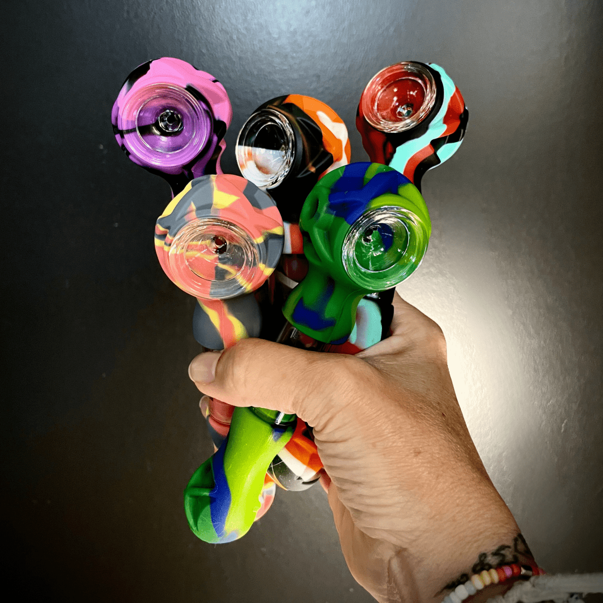 A hand holds the Hybrid Silicone and Glass Spoon with Translucent Chamber, showing its colorful design against a dark background.