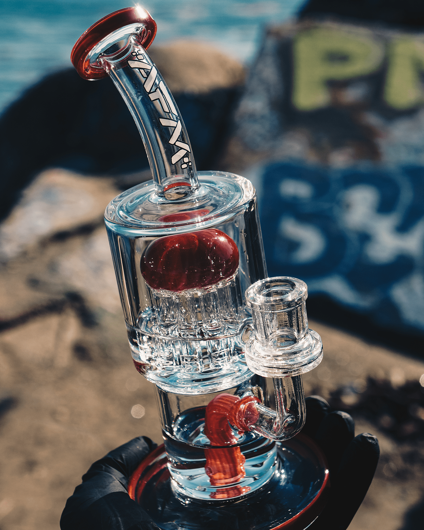 A close-up, angled view of the 9" Groovy Tree Arm Perc Dab Rig, showcasing its clear glass construction against a blurred, colorful background.