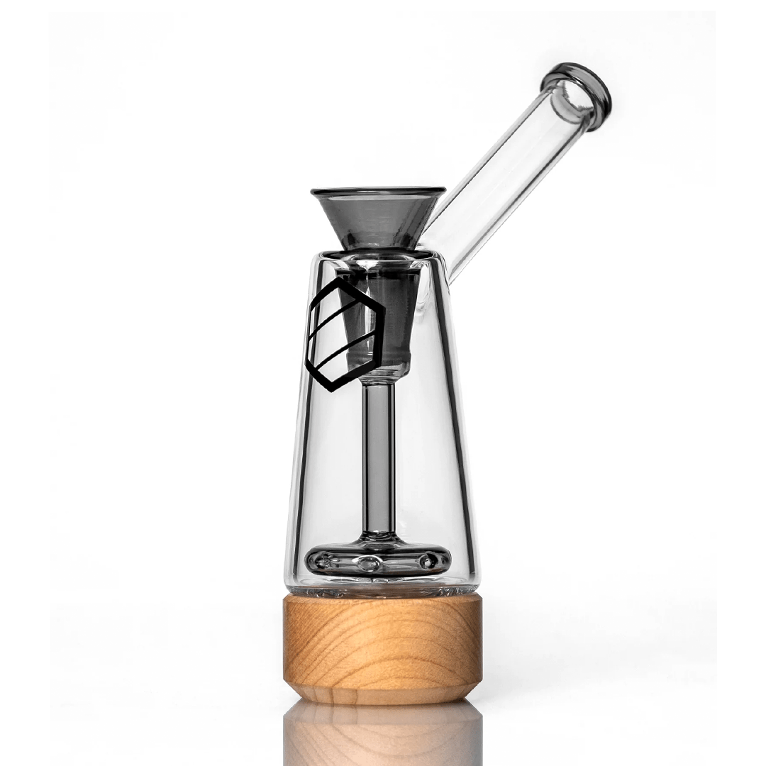 A front view of the Anomaly Drift Bubblers, showing the clear glass bubbler with a wooden base reflecting on a glossy surface.