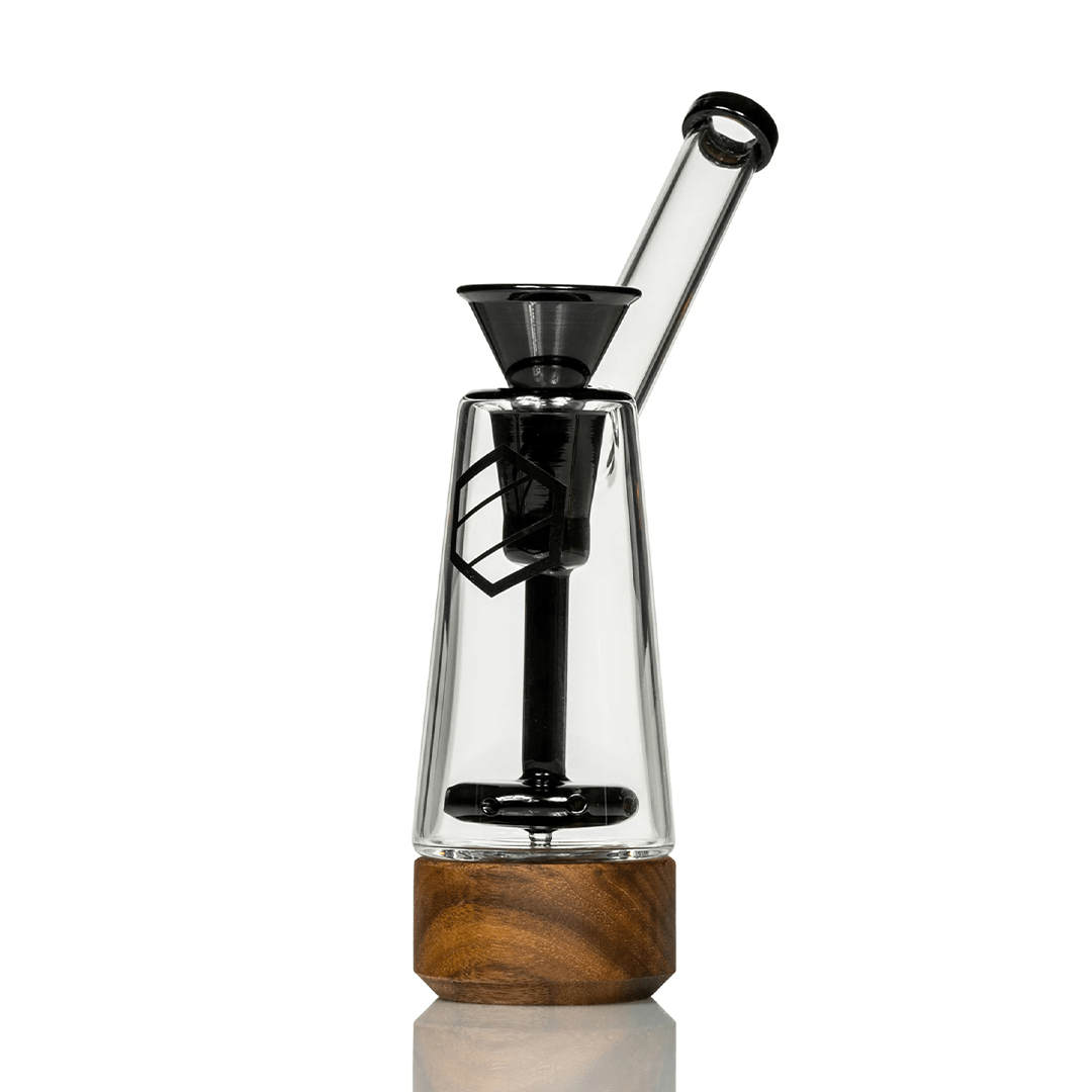 A three-quarter view of the Anomaly Drift Bubblers, featuring a clear glass piece with a wooden base on a reflective surface.